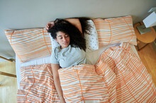 Young Woman Sleeping With Hand Behind Head On Bed At Home