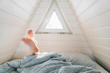 Sunlight Passing Through Window On Legs Of Woman Resting On Bed In Attic