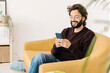 © Westend61 - Happy man wearing eyeglasses using smart phone sitting on sofa at home