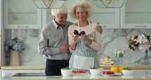 Older Wife Juggle Avocados Flirting Standing In Modern Kitchen With Beloved Husband, Spouses Talking Look Happy. Healthy Eating, Keep Balanced Diet, Byers Of Fresh Natural Delivered Products Concept