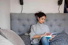 Young Woman Sitting On Sofa And Reading Book