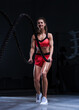© andy_gin - Athletic woman in red shorts and top exercising with ropes in functional training area. Fitness concept.