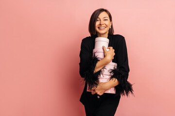 Wall Mural - Pretty young caucasian brunette girl happy birthday receives gift on pink background. Lady with smile on her face wears black pajamas. Concept of celebration, happiness and emotions.