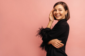 Sticker - Fair-skinned young girl with snow-white smile looks at camera while standing sideways on pink background. Brunette with bob haircut wears black pajamas. Comfortable clothes for healthy sleep.