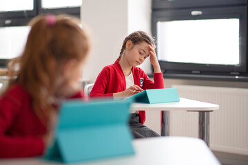 Wall Mural - Bored schoolgirl using digital tablet during lesson in classroom at primary school.