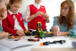 © Halfpoint - Group of kids with young science teacher programming electric toys and robots at robotics classroom