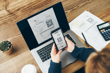 Woman scanning QR code from invoice to make payment using fast secure payment system and smartphone code reader. Business woman paying bills using express payment technology. Female using mobile phone