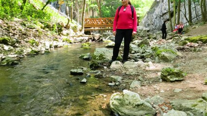 Wall Mural - Portrait of smiling woman hiker, enjoying impressive natural landscape, standing by a clear mountain creek near imposing natural stone arches, Vratna River Canyon, eastern Serbia. 4K video footage.