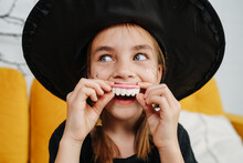 Close Up Halloween Portrait Of A Girl Witch Holding A Teeth Candy Over Mouth
