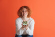 © Lustre Art Group  - Portrait of happy looking red-haired woman holding small gift box isolated over red studio background