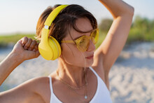 Happy Smiling Woman Listening To Music In Colorful Yellow Headphones On Sunny Beach In Summer