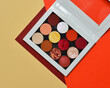 Red eyeshadow makeup palette. Realistic white case with matte, glitter, multichrome pigments. Shadows set in colors of the rainbow. Top view flat lay package isolated on green background.