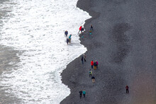 People Walking On The Beach. Waves Of The Atlantic Ocean Fall On The Black Sand Of The Beach Of Iceland From A Height