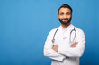 © Vadim Pastuh - Smiling Indian male doctor pediatric, physical, therapist wearing white medical gown with stethoscope on shoulders stands with arms crossed isolated on blue, copy space. Healthcare and medicine