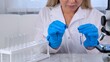 © Евгения Медведева - female research chemist scientist in a medical suit and protective gloves conducts research on samples with a micropipette and test tubes for working under a microscope in a laboratory.