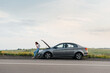 © Andrii - A young girl stands near a broken car in the middle of the highway during sunset and tries to call for help on the phone and start the car. Waiting for help. Car service. Car breakdown on the road.