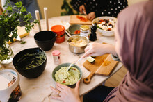 Young Woman Mixing Dipping Sauce While Preparing Food With Friends At Table