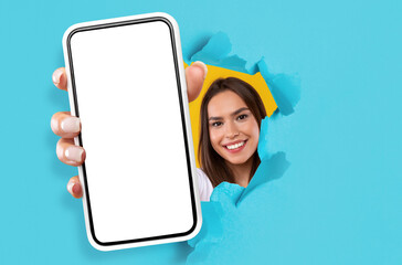 Wall Mural - young lady showing black empty smartphone screen through torn paper
