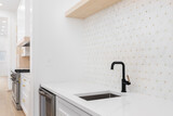Sink detail shot with a black and gold faucet, white cabinet and marble countertop, and a white and gold mosaic tile looking out towards a modern kitchen.