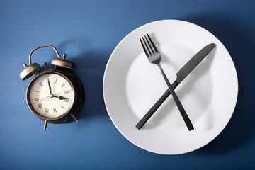 concept of intermittent fasting, ketogenic diet, weight loss. fork and knife on a plate and alarmclock