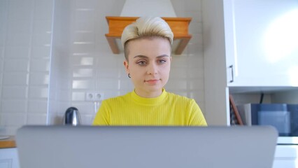 Young woman with short hair working on a computer at home. Portrait of a stylish female person with tomboy haircut using a laptop