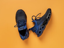 Laced Up Black Blue Mesh Fabric Sneakers Over Orange Background. Pair Of Grooved Men Shoes For Fitness And Active Lifestyle. New Fabric Sneakers With Laced Fastening. Sport Shoes Concept.