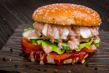 Wall Mural - Burger with meat patty, cucumbers and tomatoes with sauce on dark board