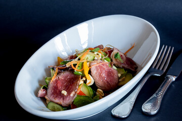 Wall Mural - Salad with roast beef with vegetables on white plate on dark table