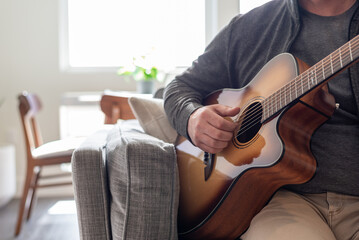 Wall Mural - Closeup of man playing acoustic guitar at home in natural light