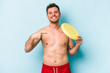 Young caucasian man playing with frisky isolated on blue background person pointing by hand to a shirt copy space, proud and confident