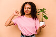 © Asier - Young African American woman holding a plant isolated on beige background feels proud and self confident, example to follow.