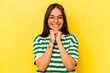 Young hispanic woman isolated on yellow background keeps hands under chin, is looking happily aside.