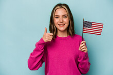 Young Caucasian Woman Holding A American Flag Isolated On Blue Background Smiling And Raising Thumb Up