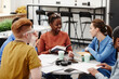 © Seventyfour - Cheerful group of young people studying together at round table in college library, focus on African American girl smiling