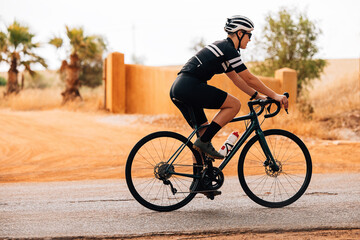 Wall Mural - Side view of female cyclist riding bicycle on countryside road. Caucasian triathlete training for competition.