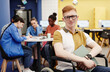 © Seventyfour - Vibrant portrait of red haired young man with disability in college library looking at camera, copy space