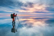 Photographer Traveler Taking Photo Of The Salt Lake At Sunset. Blue Sky With Clouds Are Reflected In The Mirror Water Surface. Professional Photographer Using Tripod And Dslr Camera