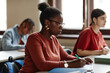 © Seventyfour - Side view portrait of African American young woman taking notes while studying at desk in school or college classroom