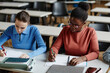 © Seventyfour - High angle portrait of African American young woman taking notes while studying at desk in college classroom