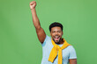 Young excited man of African American ethnicity 20s in blue t-shirt doing winner gesture celebrate clenching fists say yes isolated on plain green background studio portrait. People lifestyle concept.