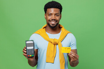 Wall Mural - Young fun man of African American ethnicity 20s wear blue t-shirt hold wireless modern bank payment terminal to process acquire credit card payments isolated on plain green background studio portrait