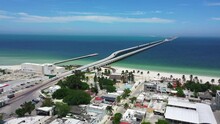 Aerial Drone Footage Of A Shipping Pier With Trucks Driving On It, Jetting Out Over The Water.  Coastal Beach Town Seen In The Foreground.