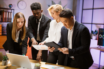 Wall Mural - Multi-ethnic group of four motivated business people working together on new project, using gadgets and reports, sharing creative ideas. Concept of teamwork and cooperation