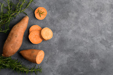 Raw whole orange sweet potato and slices of batatas with fresh rosemary on grey concrete background, top view, copy space, flat lay