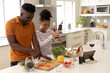 © Wavebreak Media - Smiling african american young couple with wine and digital tablet on kitchen island preparing food