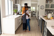 © Wavebreak Media - Side view of romantic african american young couple embracing while standing in kitchen at home