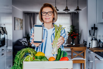 Wall Mural - Woman holding a phone with blank white screen for copy space and fresh asparagus bunch. New Start of a healthy lifestyle, weight loss. Healthy food delivery, recipe box. Selective focus