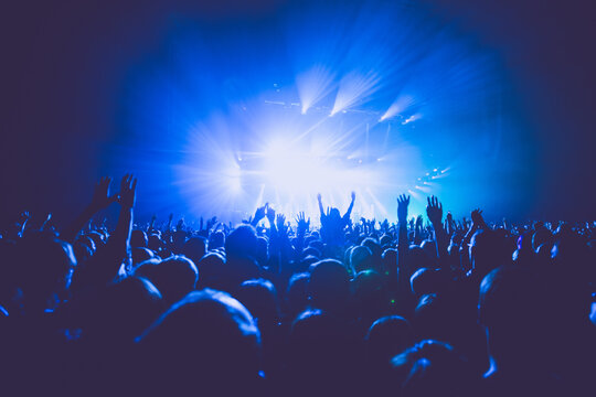 a crowded concert hall with scene stage lights in blue tones, rock show performance, with people sil