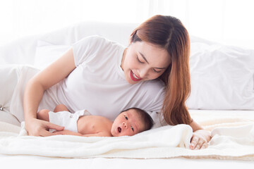 Wall Mural - Beautiful asian mother and toddler lying in bedroom talking or singing together. Singlemom watching her son with love and tender. Mom playing with cute newborn baby and spend time together on bed.