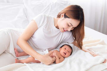 Wall Mural - Beautiful asian mother and toddler lying in bedroom talking or singing together. Singlemom watching her son with love and tender. Mom playing with cute newborn baby and spend time together on bed.